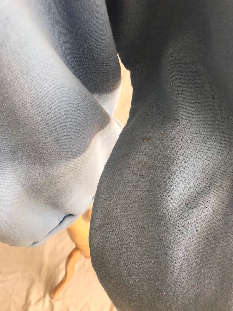 May include: Close-up of a light blue sweatshirt with a darker blue hue on the sleeve. The fabric has a soft, textured appearance.
