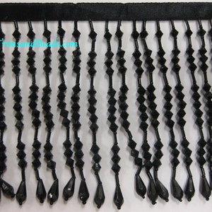 May include: Black beaded fringe trim with a teardrop shape at the end of each strand. The fringe is attached to a black ribbon.