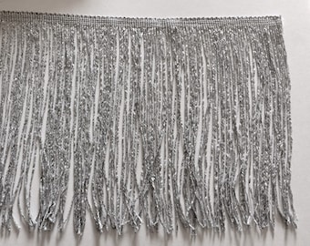 Puede incluir: Flecos plateados con borde superior tejido. Los flecos están hechos de finos hilos metálicos, creando un efecto brillante. El adorno es adecuado para embellecer ropa, accesorios o proyectos de decoración del hogar.