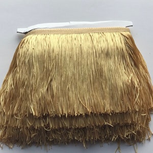 Puede incluir: Flecos dorados con múltiples capas de hebras largas y finas. El ribete tiene un respaldo beige y una tira adhesiva blanca. Este ribete decorativo es adecuado para varios proyectos de artesanía y diseño.