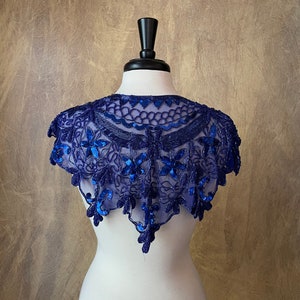 以下が含まれることがあります： 繊細な花柄が施された、ロイヤルブルーのビーズをあしらったショール。ショールは透き通るような生地で、縁は波打っています。