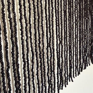 Könnte beinhalten: Eine schwarze Perlenfransenborte mit mehreren vertikalen Strängen aus kleinen, gleichmäßigen schwarzen Perlen, die an einem festen schwarzen Stoffband befestigt sind. Die Stränge hängen gerade herab und bilden ein gleichmäßiges Muster.