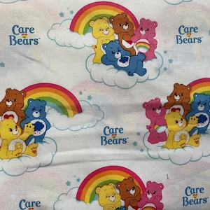 Puede incluir: Una tela blanca con un patrón repetido de osos cariñosos. Cada oso cariñoso sostiene un arcoíris y está rodeado de nubes y estrellas. El texto "Care Bears" se repite en toda la tela.