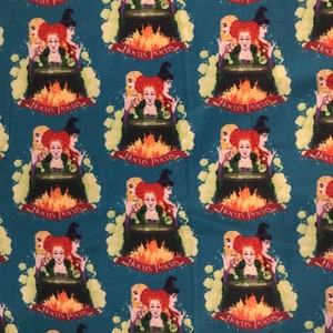 May include: A teal fabric with a repeating pattern of three witches standing around a cauldron with flames. The witches are wearing black hats and dresses with green accents. The text "Hocus Pocus" is repeated throughout the fabric.