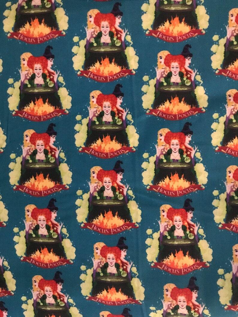 May include: A teal fabric with a repeating pattern of three witches standing around a cauldron with flames. The witches are wearing black hats and dresses with green accents. The text "Hocus Pocus" is repeated throughout the fabric.