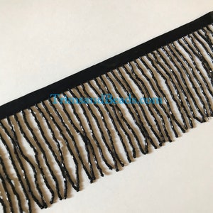 May include: Black beaded fringe trim with a black backing. The fringe is made of small, round beads that are strung together to create a long, flowing fringe.