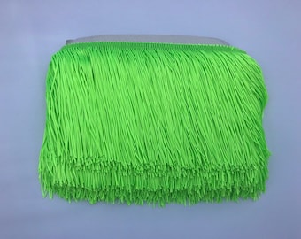 Puede incluir: Una cinta de flecos de color verde brillante con una textura lisa y uniforme. Los flecos tienen aproximadamente 2,5 cm de largo.