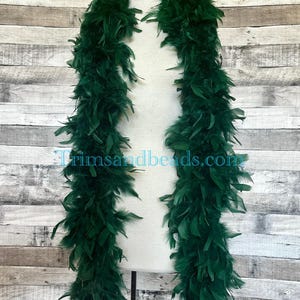 May include: A dark green feather boa displayed on a mannequin. The boa is made of soft, fluffy feathers in a deep green hue. The text "Trimsandbeads.com" is visible at the bottom of the image. This boa is a decorative accessory.