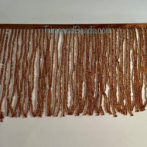 May include: Gold beaded fringe trim. The fringe is made of small, round beads that are strung together to create a long, flowing fringe. The fringe is approximately 1 inch wide and is perfect for adding a touch of elegance to any project.