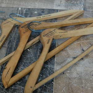 Puede incluir: Cuatro perchas de madera con diferentes etiquetas. Las perchas son de madera natural y tienen un dise&ntilde;o sencillo. Las etiquetas incluyen "The Roosevelt", "Hennig Clothing Co.", "Robert Sievert Tailors" y "New Orleans".