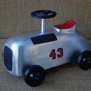 May include: A silver toy car with black wheels and a red seat. The car has a black steering wheel and the number 43 on the side.