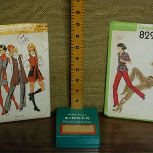 May include: Three vintage Simplicity sewing patterns, two with women's clothing designs and one with a skirt marker. The patterns are numbered 5155, 8296, and feature a Singer skirt marker.