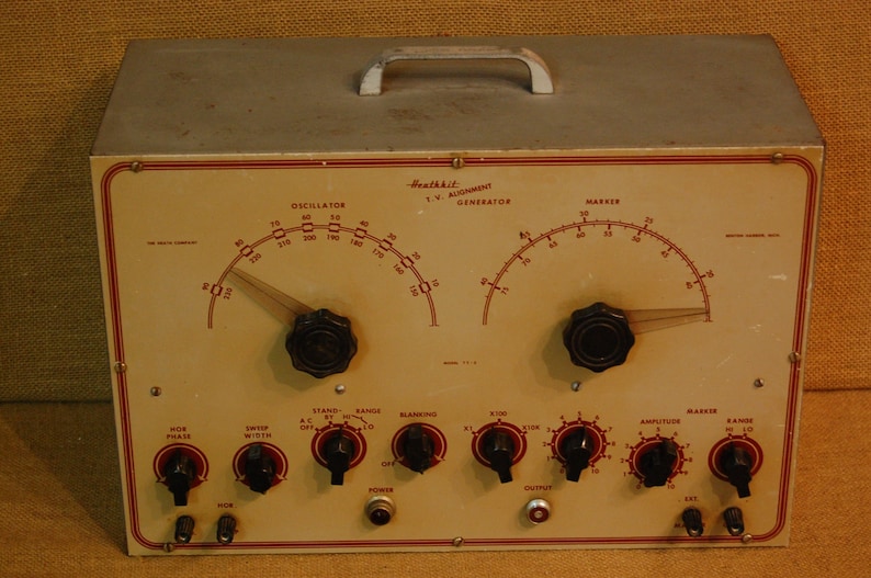May include: A Heathkit T.W. Alignment Generator with a white face and red and black markings. The front panel has two dials, knobs, and switches. The dials are labeled "Oscillator" and "Marker". The knobs are labeled "Sweep Width", "Stand By", "Range", "Blanking", "X10", "X100", "Amplitude", "Marker", and "Range". The switches are labeled "A.C. Off", "Power", and "Output".