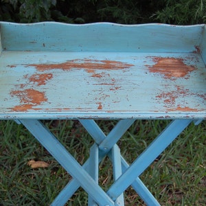 Op de afbeelding: Een blauwe houten opklapbare dienbladtafel met een verweerde afwerking. De tafel heeft een rechthoekig blad en een kruisvormig onderstel.