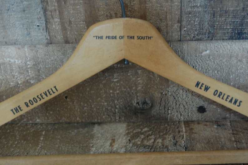 Puede incluir: Percha de madera con el texto "The Pride of the South" impreso en la parte superior y "The Roosevelt New Orleans" impreso en los lados.