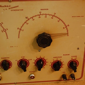 May include: A vintage Heathkit T.V. Alignment Generator with a large dial and multiple knobs. The dial is labeled "Marker" and has numbers from 25 to 75. The knobs are labeled "Stand", "Range", "Blanking", "X100", "X10K", "Amplitude", and "Marker".