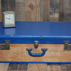 May include: A vintage blue and wood suitcase with a metal handle and two metal clasps. A small silver clock is sitting on top of the suitcase.