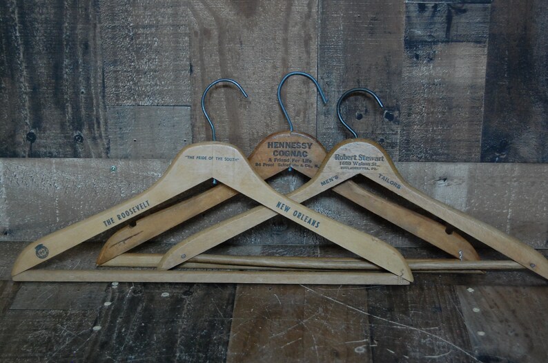 Puede incluir: Tres perchas de madera con ganchos de metal. Las perchas est&aacute;n etiquetadas con "The Roosevelt", "The Pride of the South" y "New Orleans". La percha del medio tiene una etiqueta que dice "Hennessy Cognac, A Friend For Life".