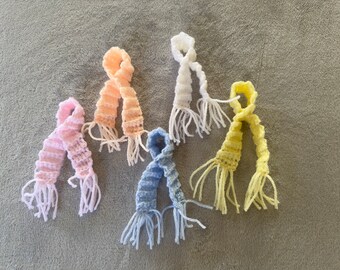 May include: Five crocheted scarves in different colors: pink, peach, white, light blue, and yellow. Each scarf has a fringe at the ends.