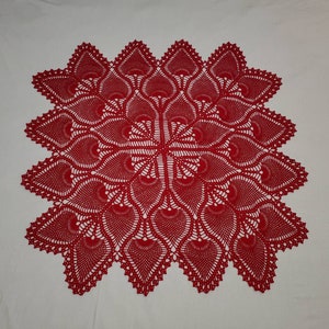May include: A red crocheted doily with a delicate, intricate design. The doily is circular and features a central motif surrounded by repeating patterns.
