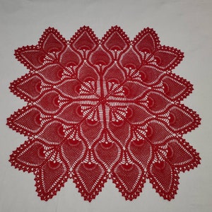 May include: A red crocheted doily with a delicate, intricate pattern. The doily is square shaped and has a scalloped edge.