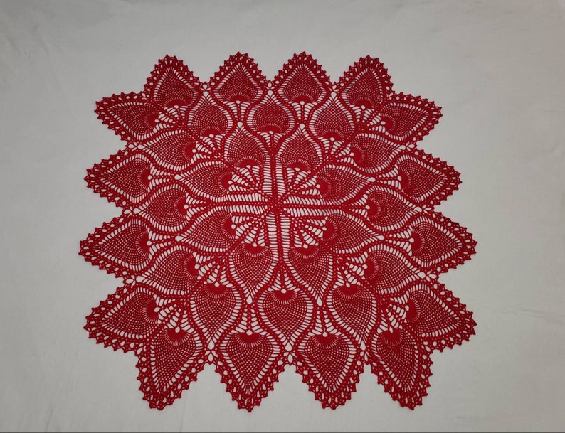 May include: A red crocheted doily with a delicate, intricate pattern. The doily is square shaped and has a scalloped edge.