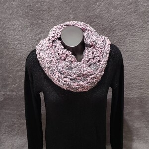 May include: A pink and gray crocheted infinity scarf. The scarf is made with a chunky yarn and has a simple, textured stitch.