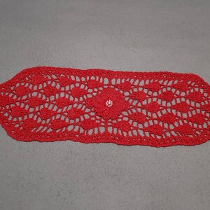 May include: Red crocheted table runner with a delicate floral pattern and white bead accents.