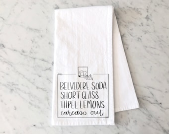Könnte beinhalten: Weißes Küchentuch mit schwarzem Text, der "Belvedere Soda Short Glass Three Lemons Carcasso Out" lautet. Der Text ist in einer handschriftlichen Schriftart gehalten und von einem schwarzen Rahmen umgeben. Es gibt eine Schwarzweißillustration eines Glases mit Eis und Zitronenscheiben.