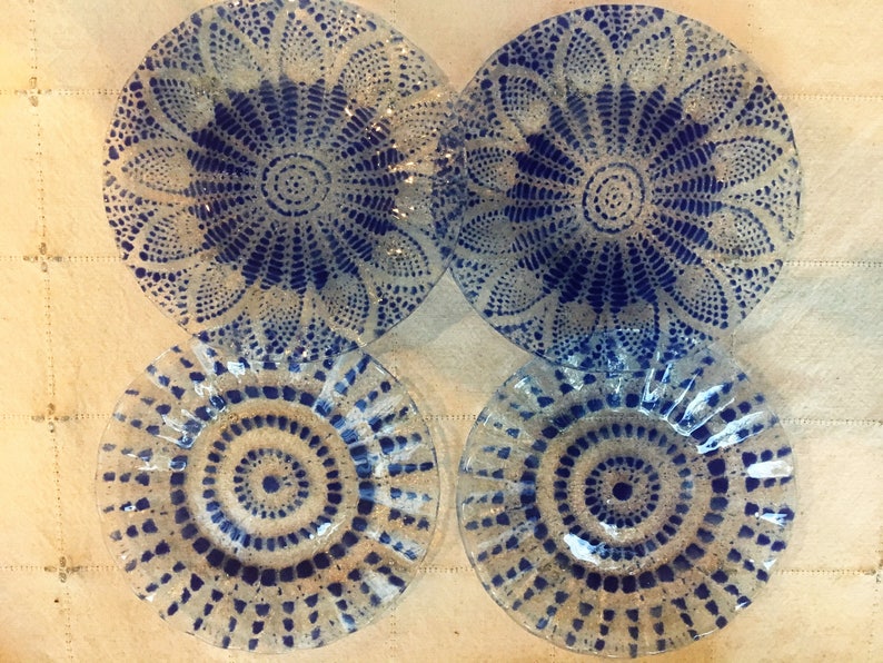 May include: Four glass plates with blue and white patterns. The plates have a scalloped edge and a circular design in the center.