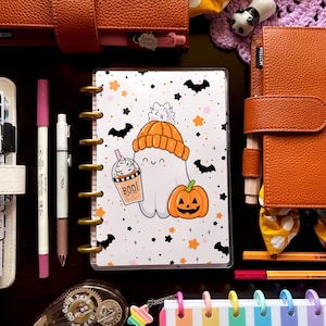 May include: A collection of stationery items, including a planner with a Halloween ghost design, pens, and decorative accessories. The planner features a cute ghost with a pumpkin and the word "BOO!". Other items include a tape dispenser, and colorful paper clips.