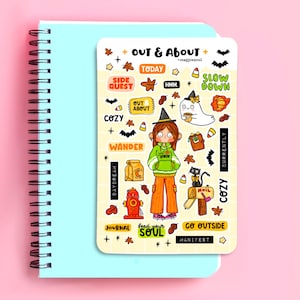 May include: A sticker sheet titled Out & About by magpiesoul featuring a central character in a witch hat and green hoodie, surrounded by autumn-themed illustrations including a ghost, black cat, fire hydrant, mailbox, and various text labels.