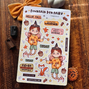 May include: A rectangular sticker sheet titled Fountain Pen Fairy featuring two illustrated fairies with wings, hats, and sweaters, surrounded by autumn-themed icons like acorns, leaves, and a fox, with text including Hello Fall, Sweater Weather, and Today.