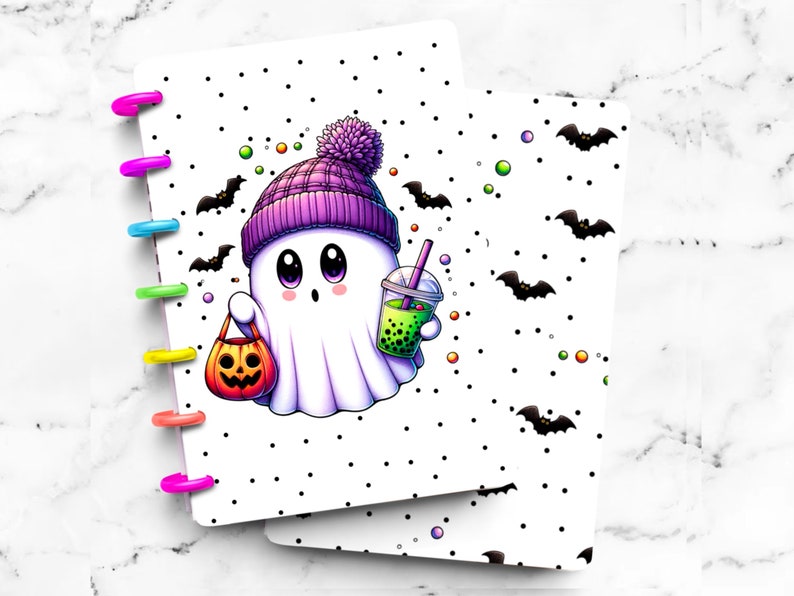 May include: A Halloween-themed planner cover featuring a cartoon ghost wearing a purple beanie and holding a pumpkin-shaped candy bag and a boba drink. The cover has a white background with black polka dots and bat illustrations. The planner rings are multi-colored.