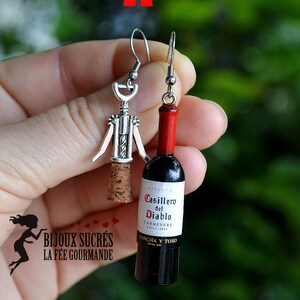 May include: A pair of silver earrings with a corkscrew and a miniature wine bottle charm. The bottle charm is labeled "Casillero del Diablo Carmenere Chile 2019 Concha y Toro".