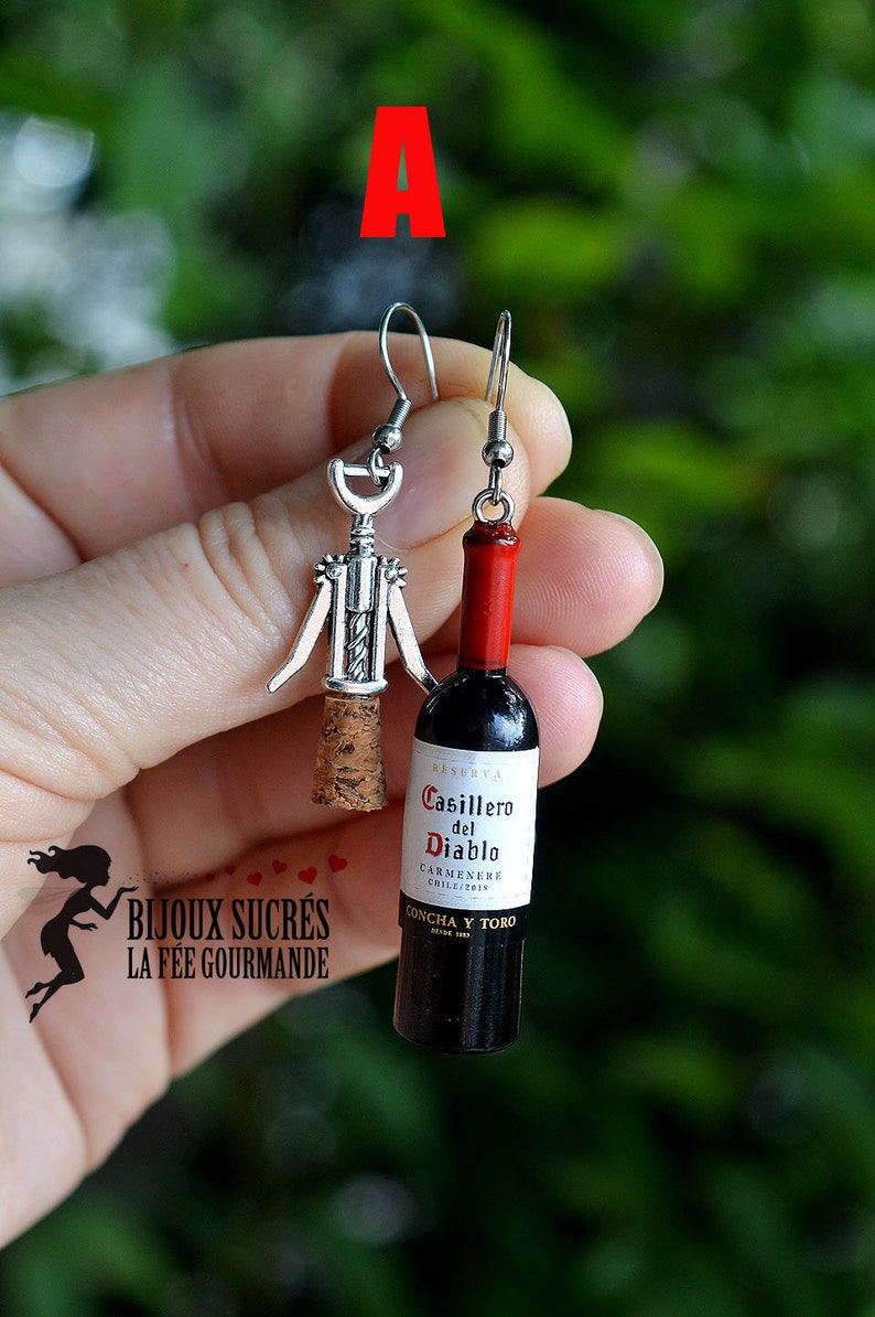 May include: A pair of silver earrings with a corkscrew and a miniature wine bottle charm. The bottle charm is labeled "Casillero del Diablo Carmenere Chile 2019 Concha y Toro".