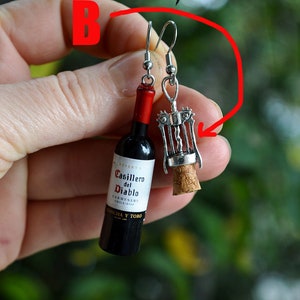 May include: A pair of earrings featuring a miniature wine bottle and a corkscrew. The wine bottle is labeled "Casillero del Diablo" and the corkscrew is silver.