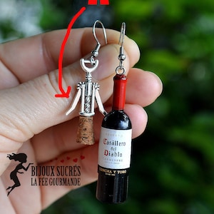 May include: A pair of earrings featuring a miniature wine bottle and a corkscrew. The wine bottle is labeled "Casillero del Diablo Carmenere Chile 2019 Concha y Toro".