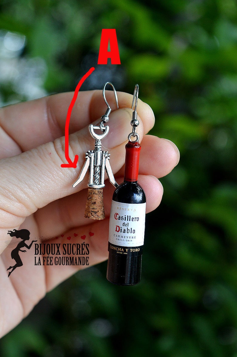 May include: A pair of earrings featuring a miniature wine bottle and a corkscrew. The wine bottle is labeled "Casillero del Diablo Carmenere Chile 2019 Concha y Toro".
