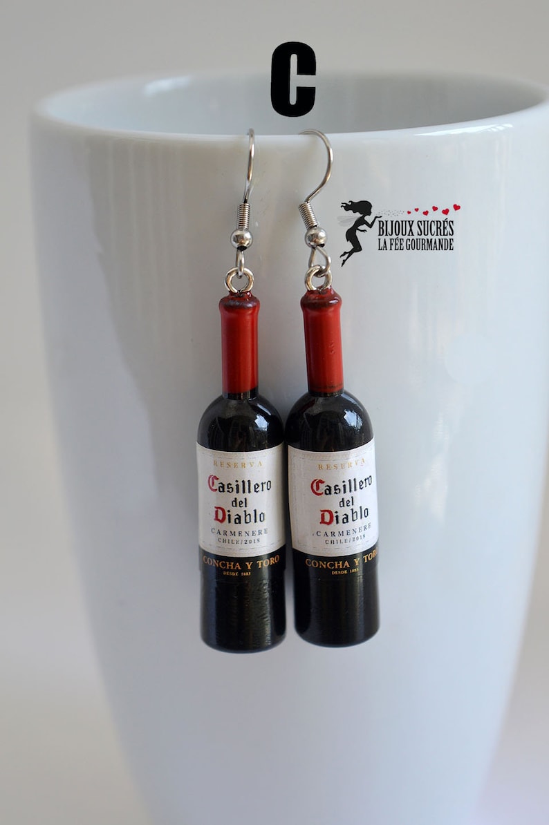 May include: A pair of earrings featuring miniature wine bottles with the label "Casillero del Diablo Carmenere Chile/2015 Concha y Toro" in black and white text on a red and black bottle.