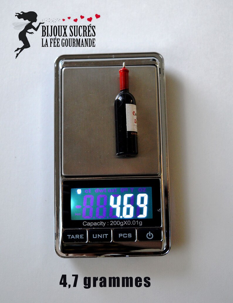 May include: A small, red wine bottle charm weighs 4.7 grams on a digital scale. The charm is labeled "C.D. Co."