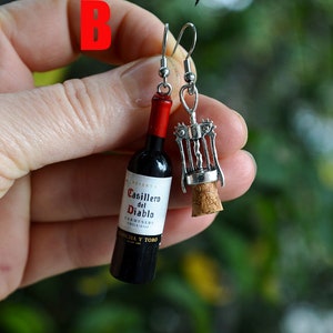 May include: A pair of earrings featuring a miniature wine bottle and a corkscrew. The wine bottle is labeled "Casillero del Diablo Carmenere Chile 2014 Concha y Toro".