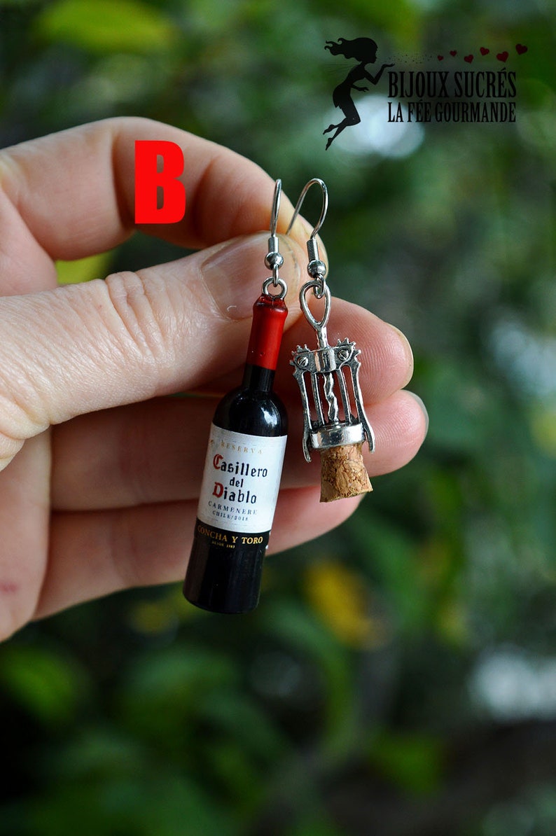 May include: A pair of earrings featuring a miniature wine bottle and a corkscrew. The wine bottle is labeled "Casillero del Diablo Carmenere Chile 2014 Concha y Toro".