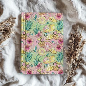 May include: A notebook with a colorful tropical fruit pattern. The design features illustrations of pineapples wearing sunglasses, lemons, pink flowers, and green leaves on a gradient pink and green background.