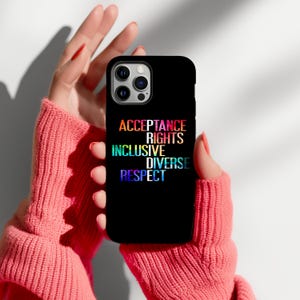 Puede incluir: Funda de teléfono negra con las palabras "ACCEPTANCE, RIGHTS, INCLUSIVE, DIVERSE, RESPECT" en colores arcoíris. La funda del teléfono la sostiene una persona que lleva un suéter rosa.