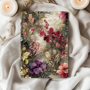 May include: A rectangular notebook with a floral design. The cover features a watercolor-style illustration of various flowers in shades of pink, purple, and yellow against a muted gray background. Faint script-like text is visible throughout the design.