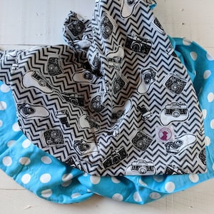 May include: A black and white fabric with a chevron pattern and vintage cameras printed on it. The fabric is bordered with a turquoise fabric with white polka dots.
