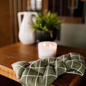 May include: A green and white checkered fabric heating pad on a wooden table. The heating pad is folded in half and has a quilted design.