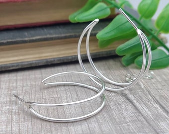 May include: A pair of silver hoop earrings with a double-hoop design. The earrings are made of a thin, smooth metal and have a simple, elegant style.