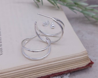 May include: Silver hoop earrings with a hammered texture and a double hoop design.